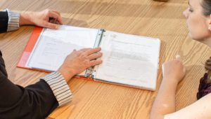 Two people look at an open book on an oak table.