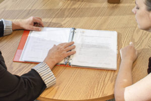 Two people look at an open book on a circular table.